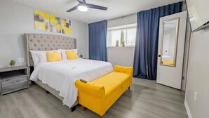 Une chambre à coucher avec un lit, un canapé jaune, un ventilateur de plafond et une fenêtre avec des rideaux.