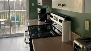 A kitchen with a stove, coffee maker, and toaster. There is a sliding glass door leading to a patio with chairs. - Cozy retreat In National Capital Region! (Gatineau)