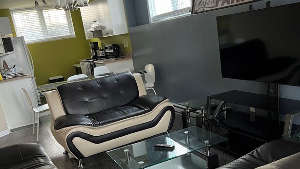 A modern living room with a sofa, a glass coffee table, and a TV. - Cozy retreat In National Capital Region! (Gatineau)