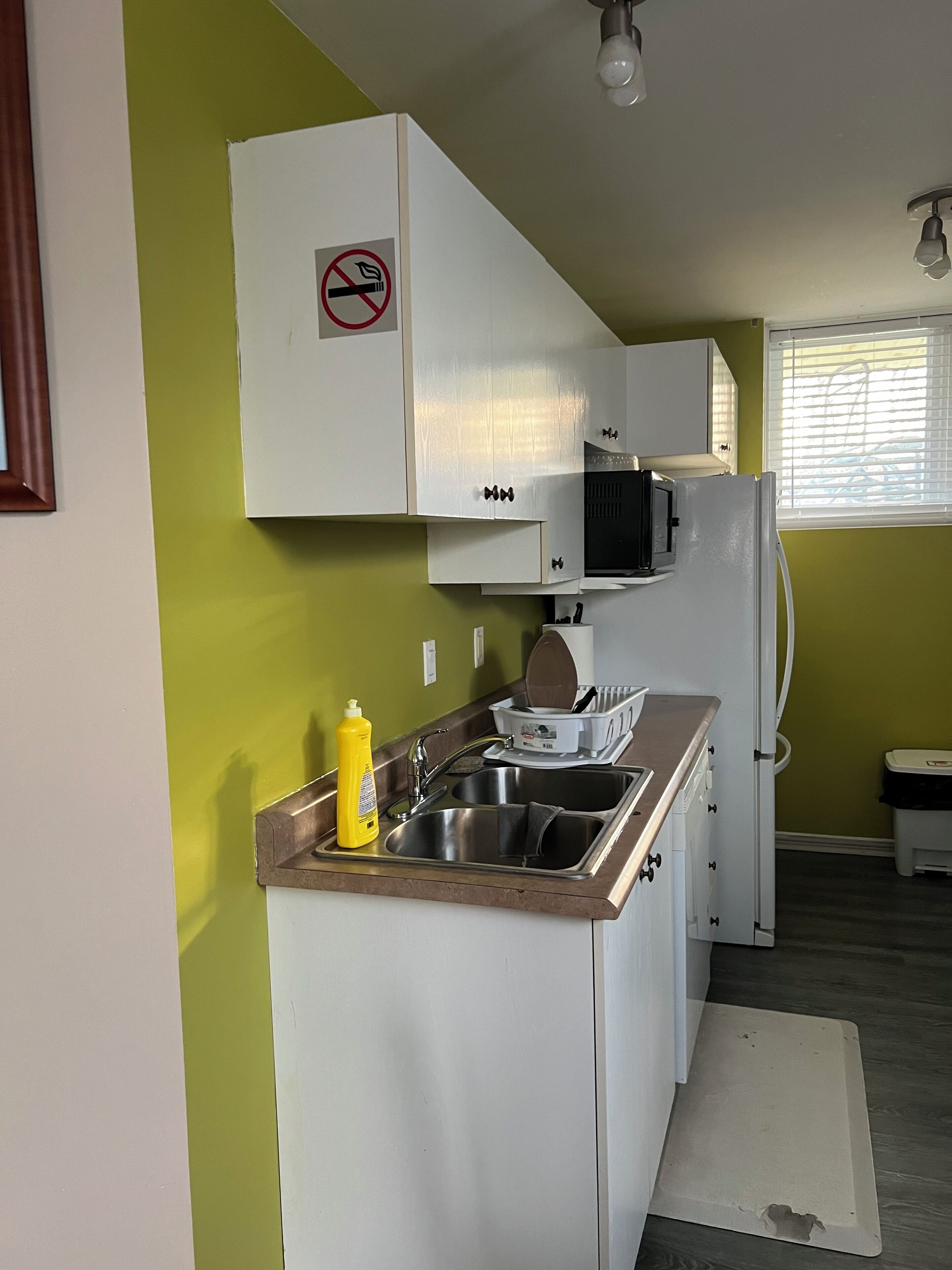 A compact kitchen with white cabinets, a stainless steel sink, and a microwave.