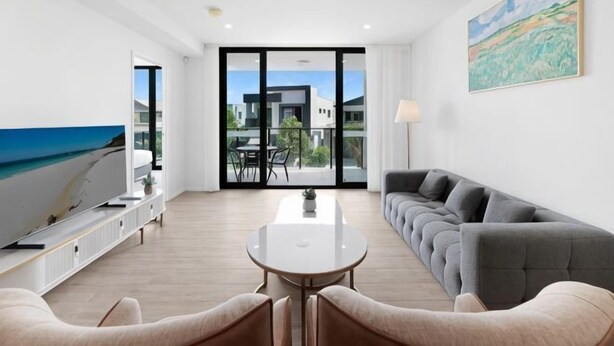 A modern living room with a sofa, a dining table, and a TV. There is a balcony with a view of the sea. - The Residences at the Peninsula (Hope Island)