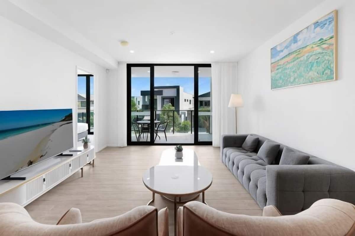 Una sala moderna con sofá, una mesa de comedor y un televisor. Hay un balcón con vista al mar.