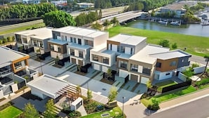 A modern residential complex with multiple two-story houses, a central courtyard, and a view of a river and bridge. - The Residences at the Peninsula (Hope Island)