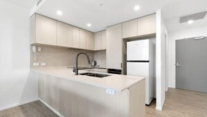 A modern kitchen with a central island, built-in appliances, and a grey door. - The Residences at the Peninsula (Hope Island)