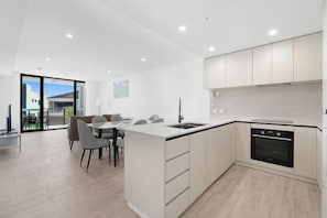 Una cocina moderna con una isla central, horno empotrado y un comedor con sillas.