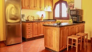 A kitchen with wooden cabinets, a stainless steel refrigerator, a built-in island with stools, and a microwave stacked on top of a toaster oven.
