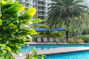 A swimming pool with lounge chairs and umbrellas, surrounded by greenery and a multi-story building. - TUI BLUE The Haven Ipoh (Ipoh)
