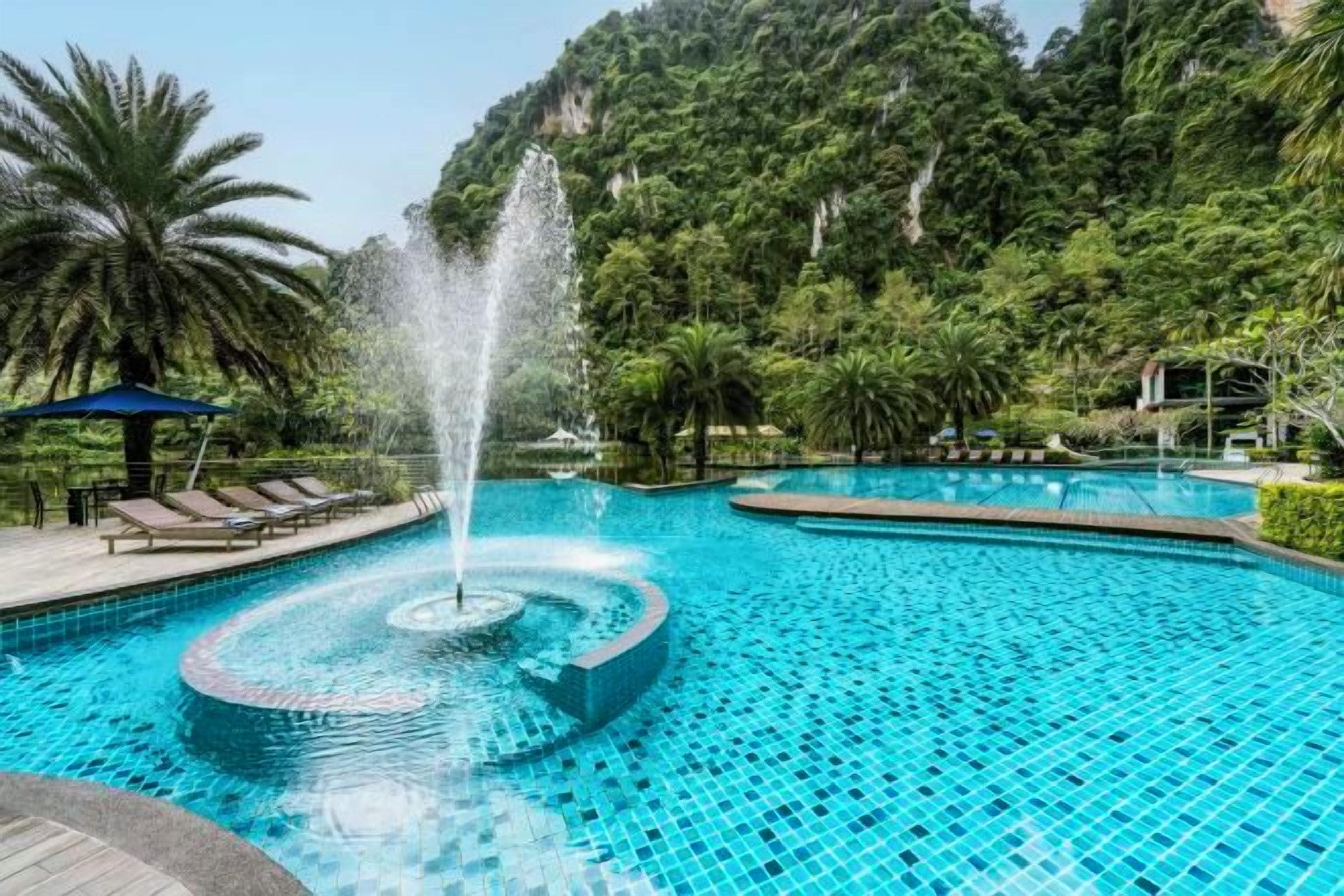 A pool with a circular water feature surrounded by lounge chairs and palm trees.