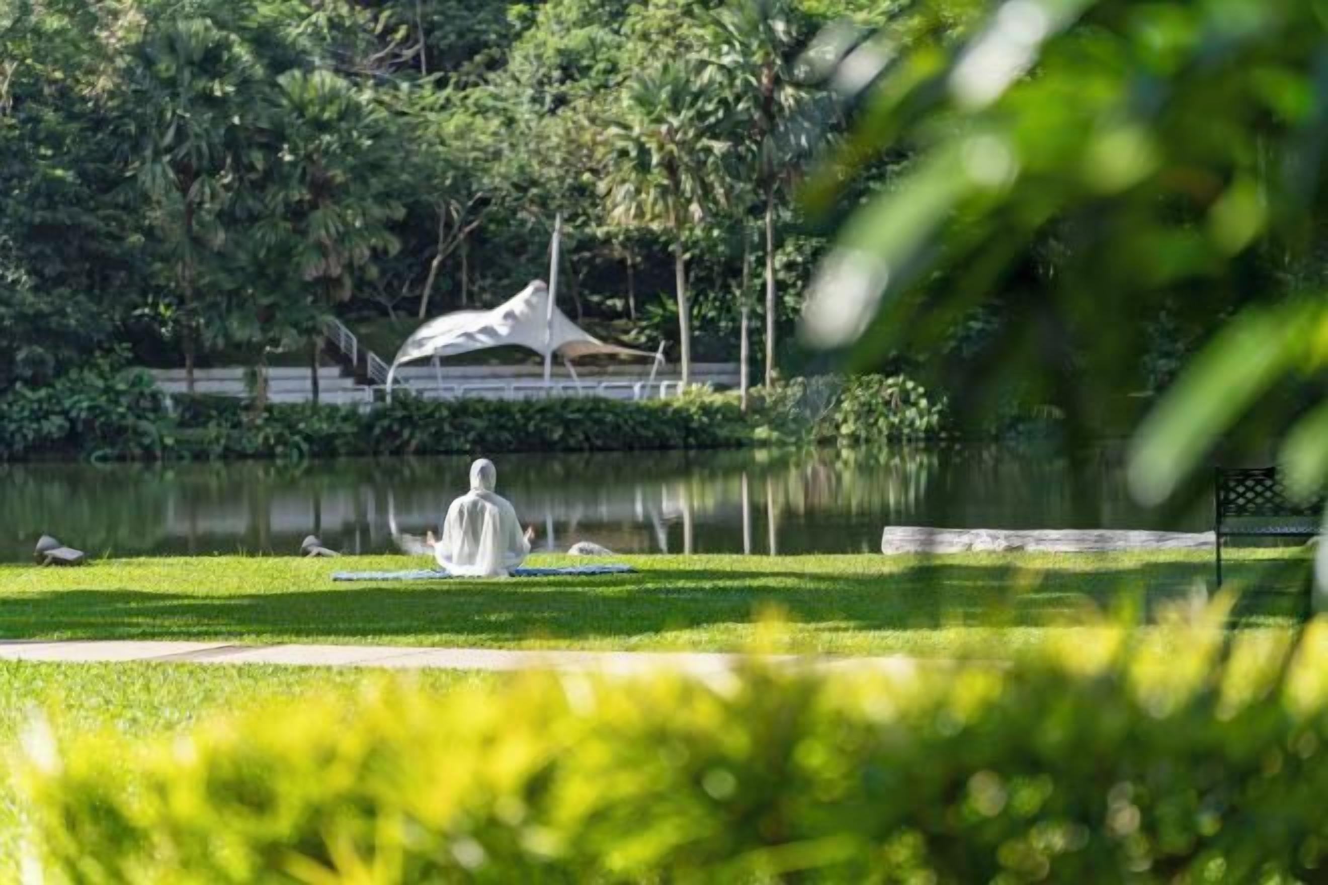 A statue in a park with a pond, trees, and a white gazebo in the background.