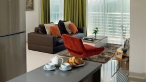 A modern living room with a sofa, a red chair, a dining table with a coffee set, and a kitchen area with a refrigerator. - TUI Blue The Haven Ipoh (Ipoh)