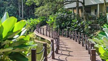 A wooden pathway with chain-link railings, surrounded by lush greenery and leading to a building.