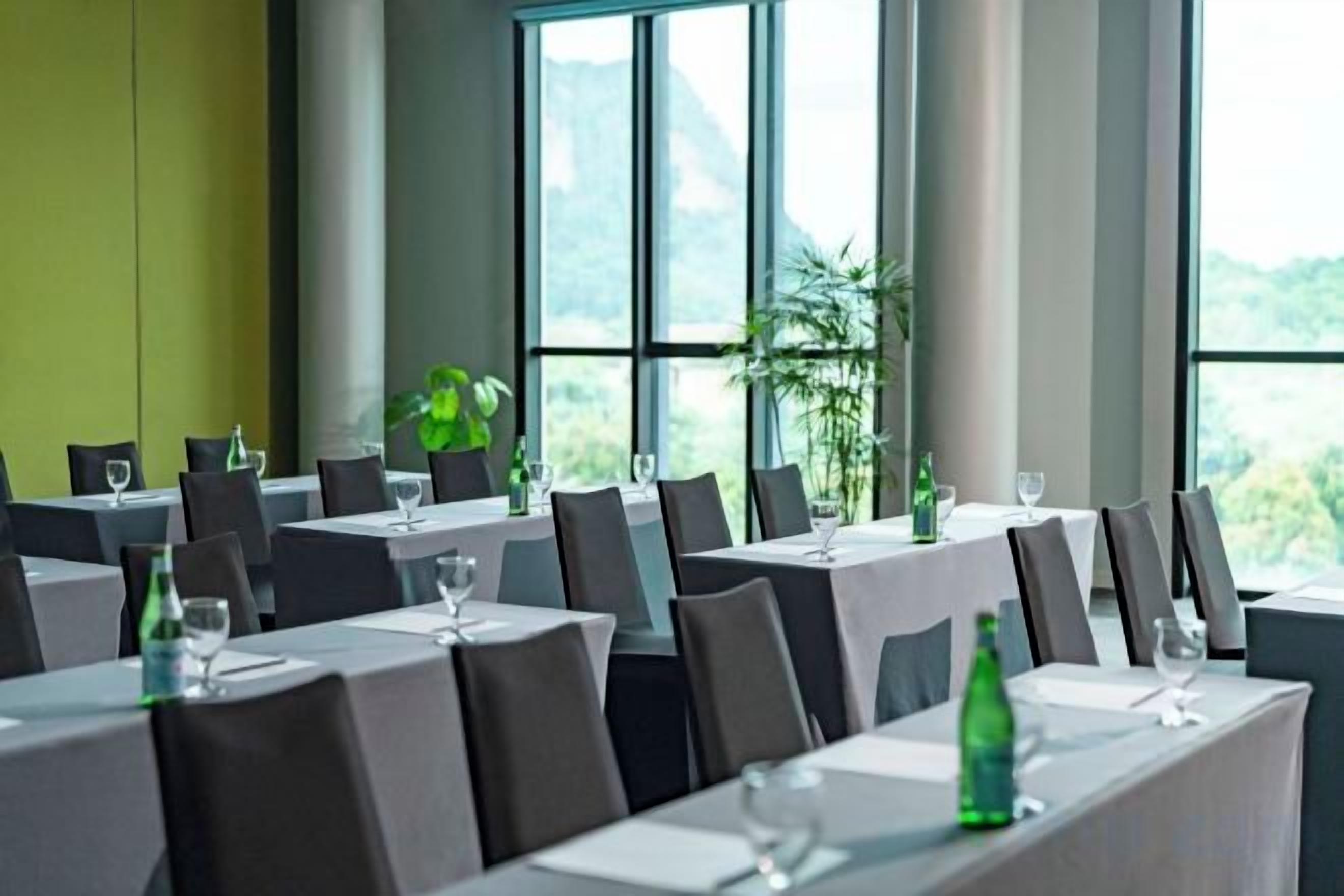 A restaurant with multiple tables set for dining, large windows, and indoor plants.