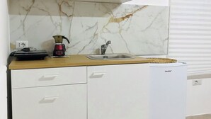 Una cocina compacta con armarios blancos, salpicadero de mármol, cafetera y un refrigerador pequeño.