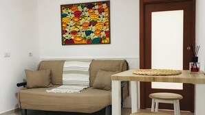 Una sala de estar con un sofá, una mesita baja con taburetes, una obra de arte colorida en la pared y un equipo de aire acondicionado.