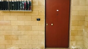 Una puerta de madera cerrada con un pequeño ventanal en la parte superior, suelo de baldosas y un dispositivo de seguridad fijado a la pared.