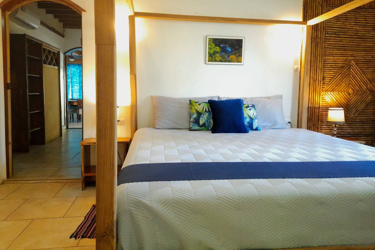 A bedroom with a bed, pillows, a picture on the wall, and a wooden headboard.