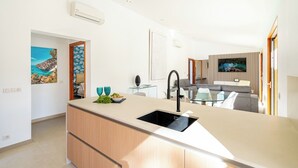Une cuisine moderne dotée d’un îlot central, un coin repas avec une table en verre et un espace de vie comprenant un canapé et un téléviseur.