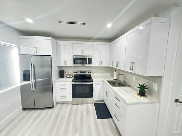 A modern kitchen with white cabinets, stainless steel appliances, and a marble countertop.
