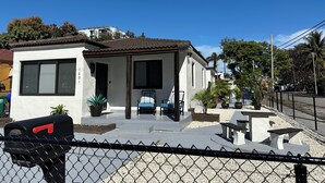 Une maison à deux étages avec un porche à l’avant, une boîte aux lettres et un petit patio aménagé avec des sièges et des jardinières.