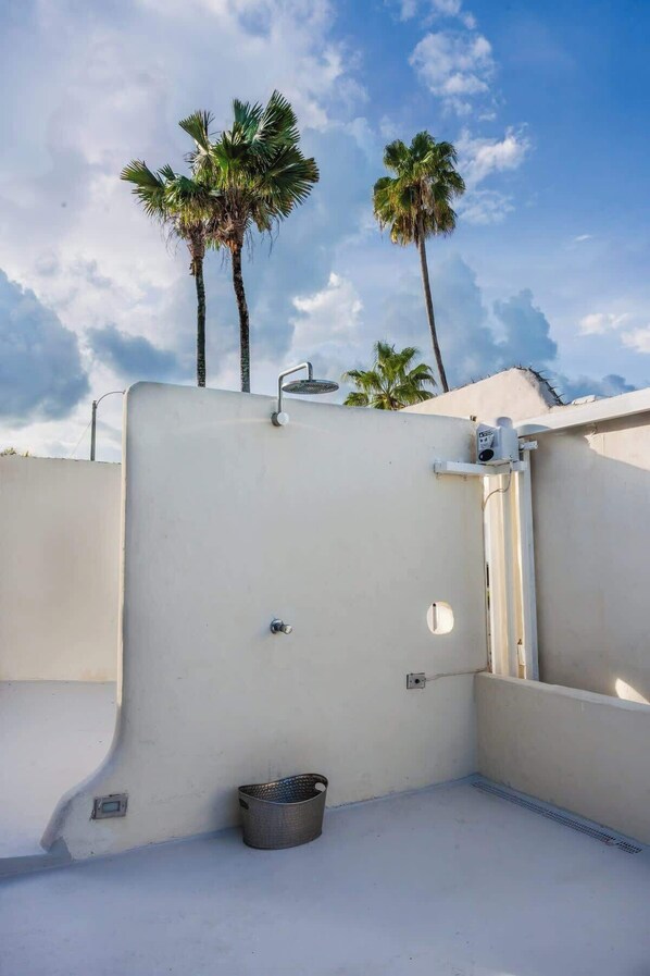 Una terraza en la azotea con un muro blanco, barandilla metálica y un balde pequeño de metal.