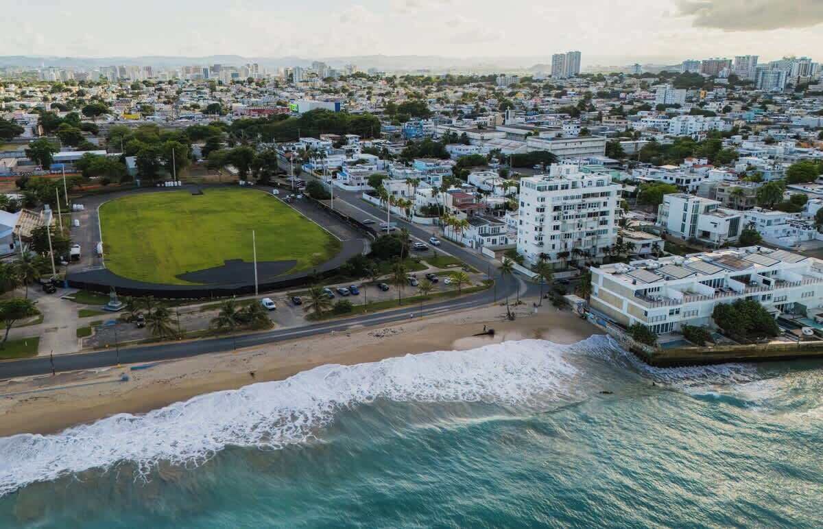 Vista aerea di una città costiera con un grande parco, spiaggia e edifici residenziali.
