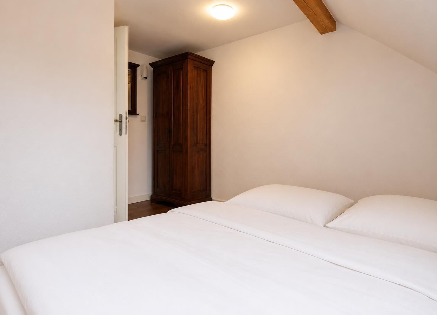 A bedroom with a bed, a wardrobe, and a door leading to another room.