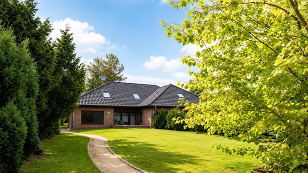 A two-story house with a paved driveway, surrounded by well-maintained grass and trees.