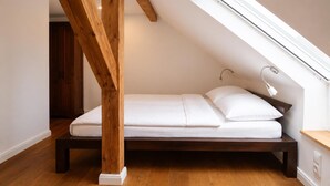 A loft bedroom with a wooden beam ceiling, a skylight, a bed, and a bedside table.