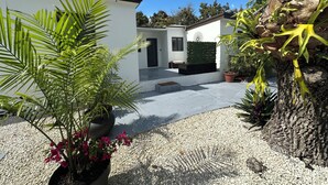 A modern outdoor area with a gravel path, potted plants, and a white building with a door and window. - Charming 1-bedroom apartment with AC, WiFi in vibrant Miami (Miami)