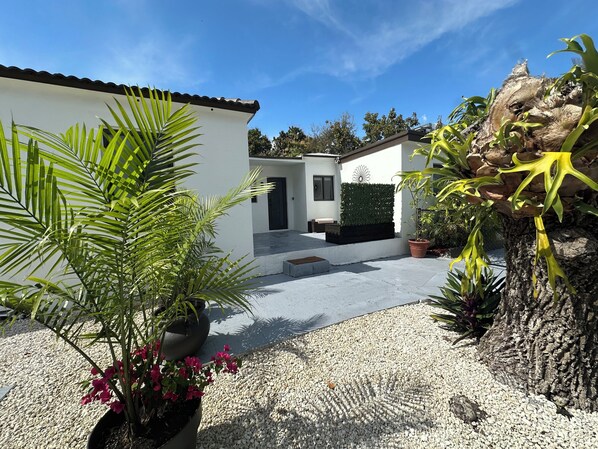 A modern outdoor area with a gravel path, potted plants, and a white building with a door and window.