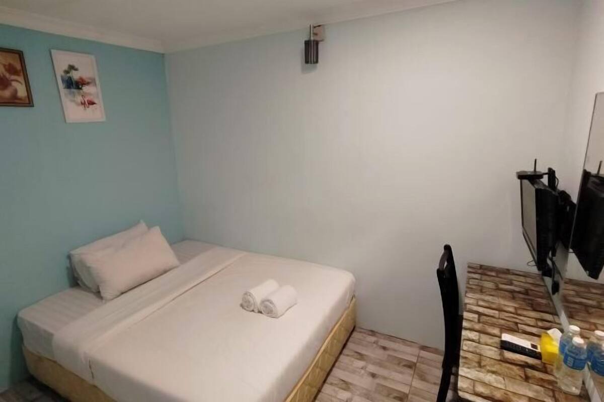 A small, clean room with a bed, a wooden table with toiletries, and a mirror.