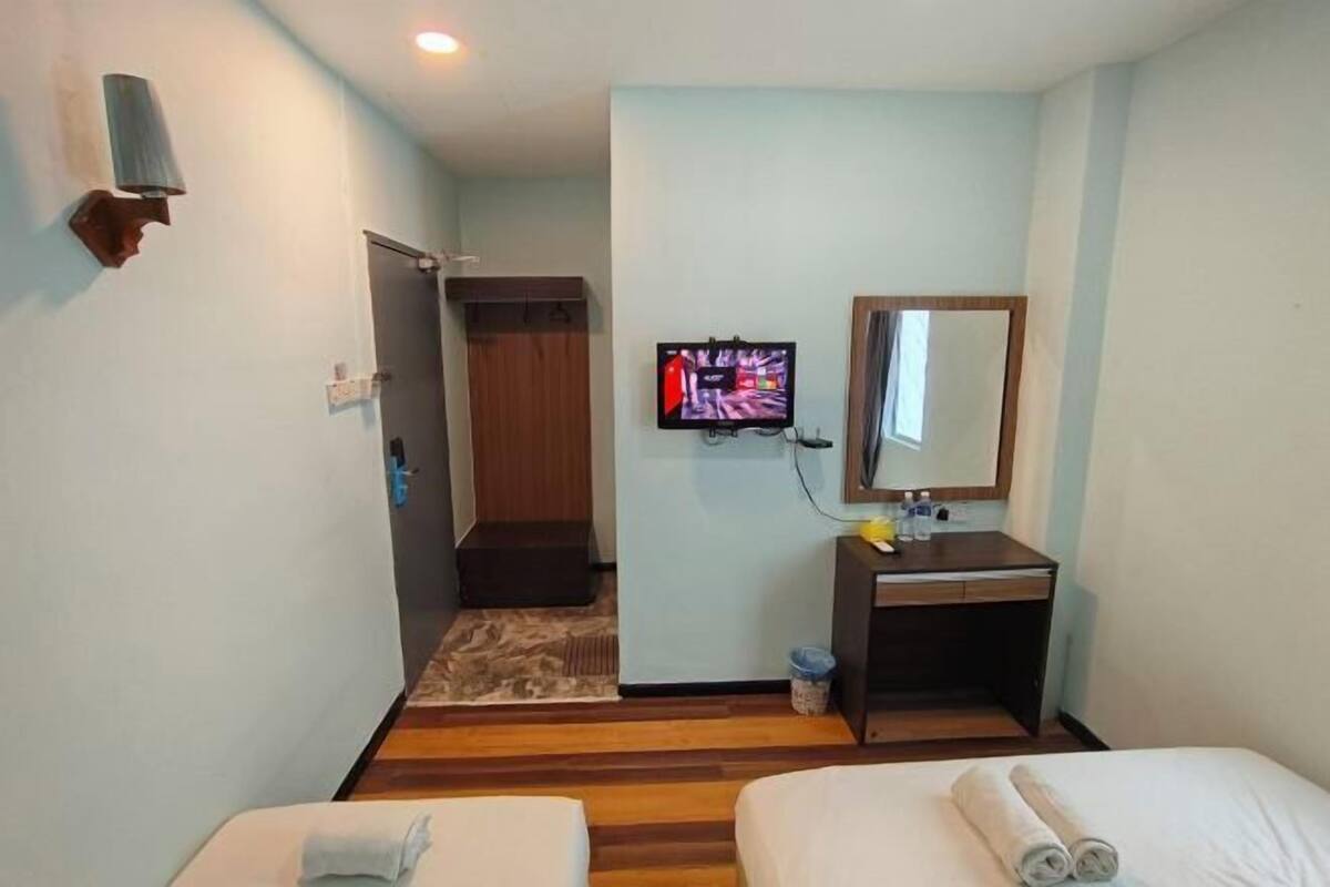 A hotel room with a bed, a desk with a mirror, a television, and a door leading to a bathroom.