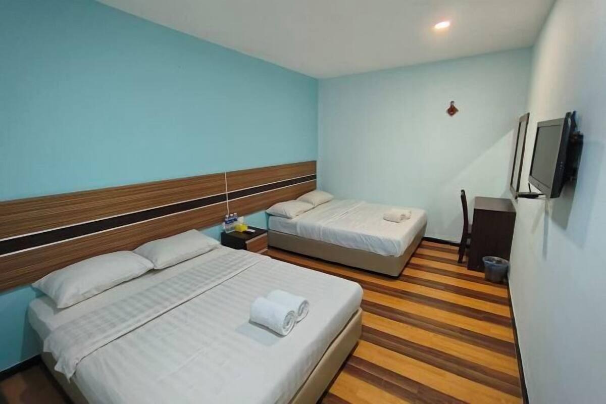 A hotel room with two beds, a wooden floor, a TV, and a small table.