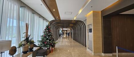 A hotel corridor with a Christmas tree, potted plants, and a seating area.