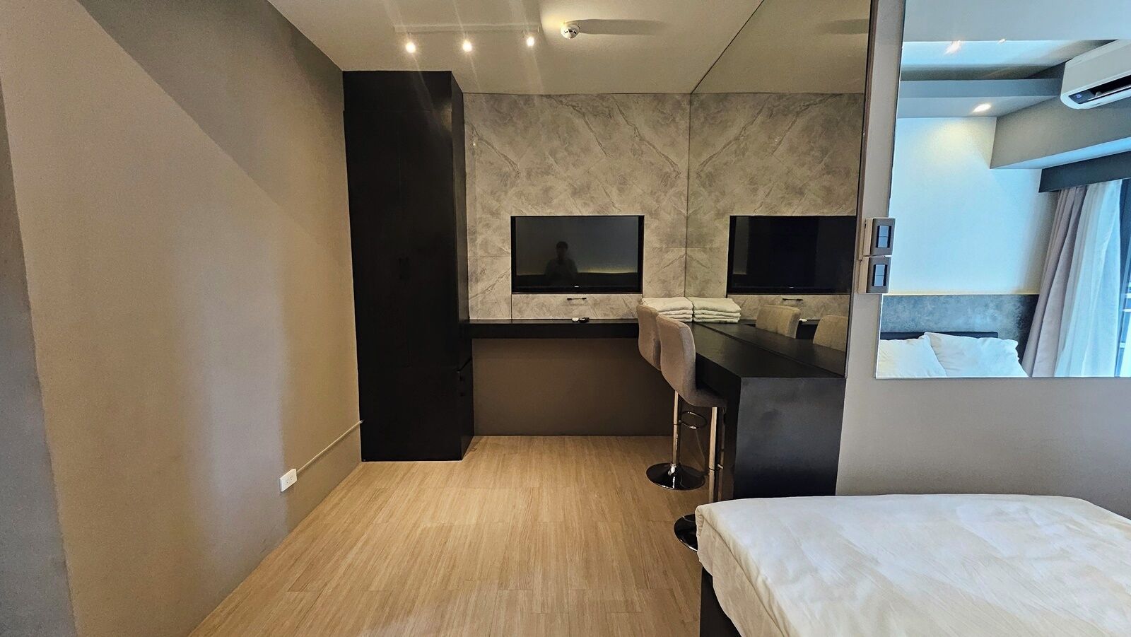 A compact hotel room with a bed, a small kitchenette, a mirror, and a window.