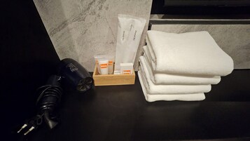 En svart hårtork, en trälåda med artiklar för munhygien och staplar av vita handdukar på en svart bänkskiva.