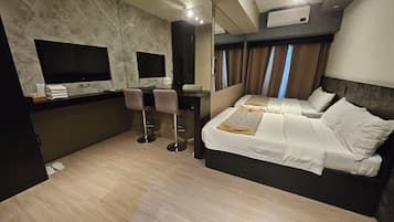 A hotel room with a bed, two chairs, a desk, a flat-screen TV, and a mirror.