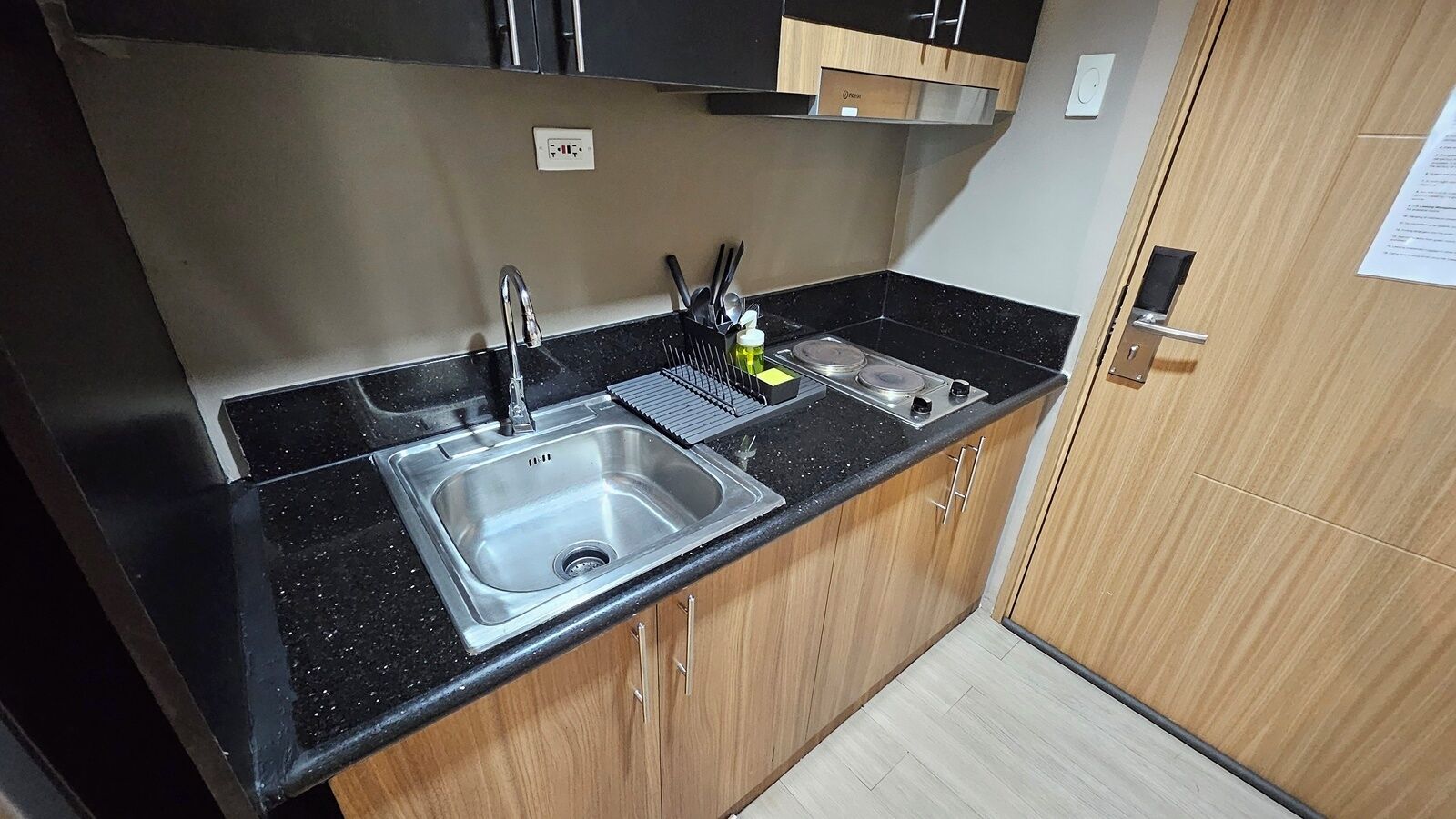 Una cocina con pileta de acero inoxidable, encimera negra y alacenas de madera.