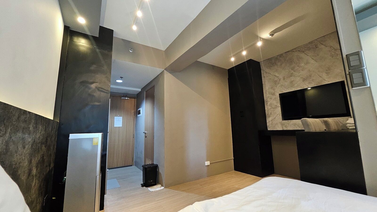 A modern hotel room with a large bed, a flat-screen TV mounted on the wall, and a wooden floor.