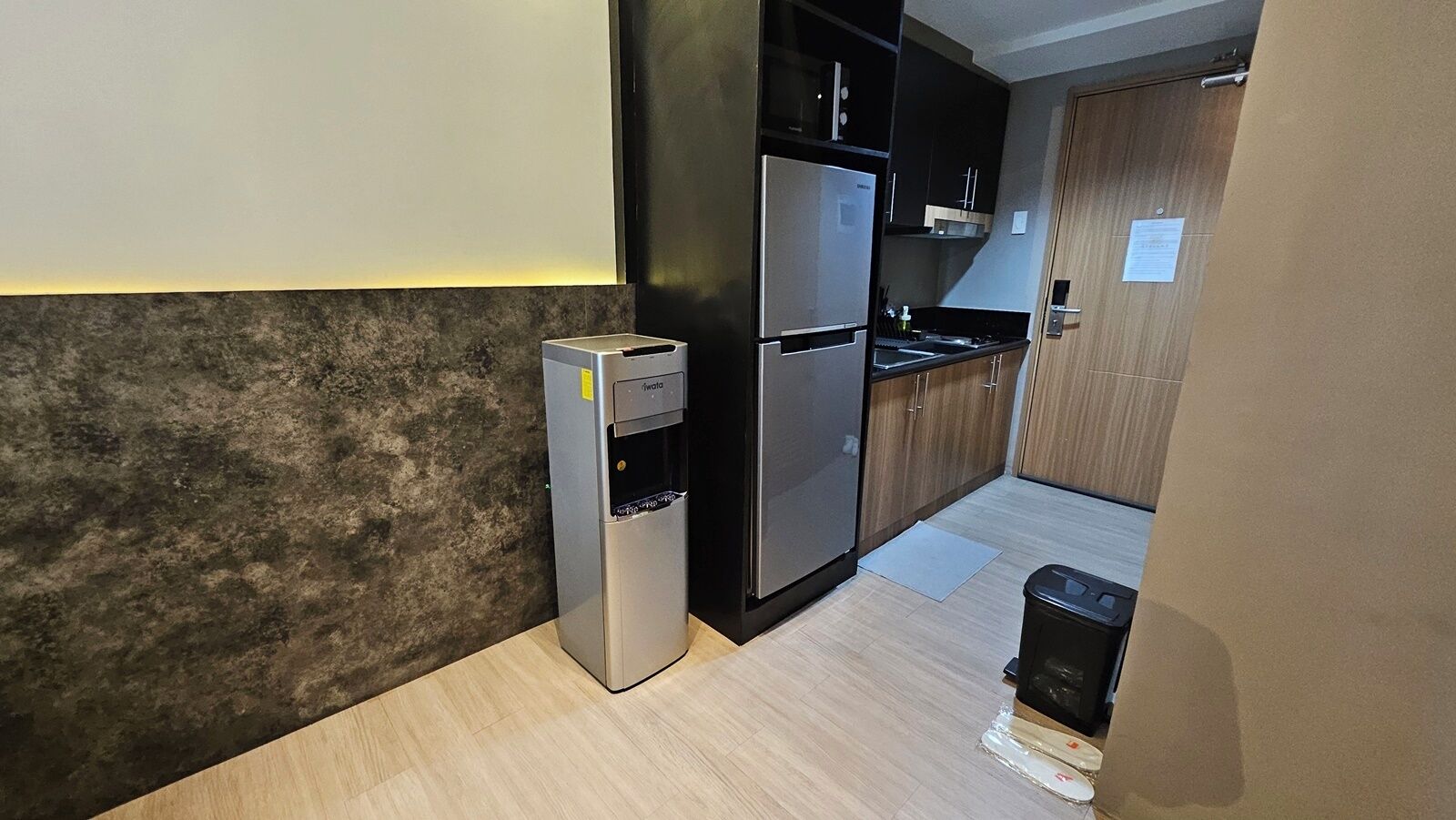 Une cuisine compacte équipée d’un distributeur d’eau, d’un réfrigérateur et d’une poubelle.