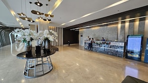 A modern lobby with a reception desk, a glass coffee table with vases, and a polished floor. - Shore 3 Residences by LUXE (Pasay)
