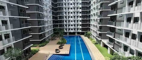 Un immeuble d’appartements moderne doté d’une piscine centrale, entouré de balcons et de verdure.