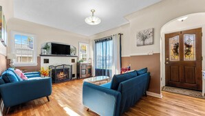 A living room with a fireplace, sofas, a television, and a view of the outside.