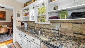A kitchen with white cabinets, granite countertops, and a window with a view of greenery.