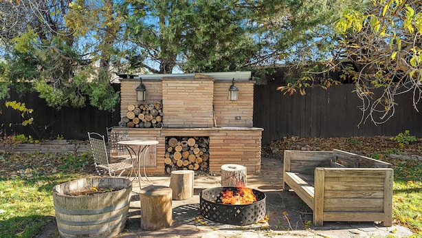 A backyard with a brick barbecue area, wooden seating, and a fire pit.