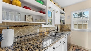 A kitchen with granite countertops, white cabinets, and a window with a view of the outside.