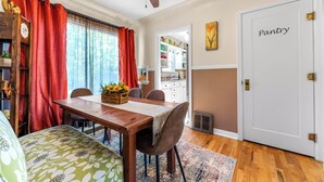A dining area with a wooden table, chairs, and a red curtain. There is a door labeled "Pantry" and a window with curtains.