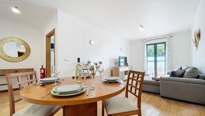 A dining area with a round wooden table, chairs, and a dining set. There is a sofa and a television in the background.