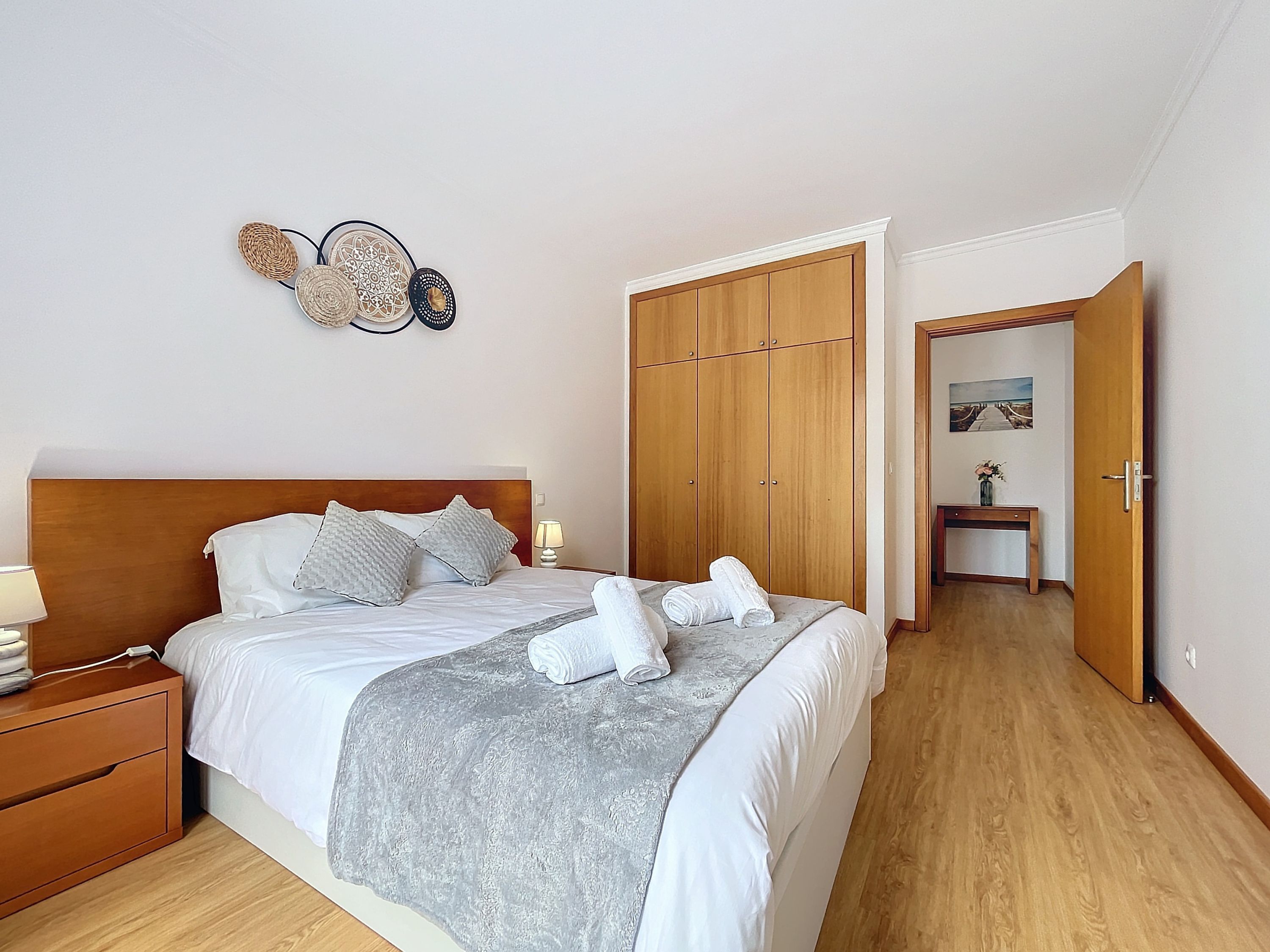 A neatly made bed with pillows and a blanket, a bedside table with a lamp, and a wooden wardrobe.