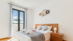 A modern bedroom with a large bed, a nightstand, a wall art piece, and a view through a sliding door.